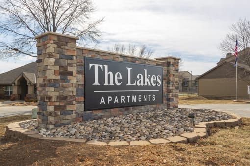 The Lakes apartment complex entrance sign with a stone-brick backing and the clubhouse visible in the background.