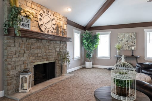 Living room with beige walls, carpet flooring, a large window, a stone fireplace, a clock on the mantel, a birdcage, and ample natural light.