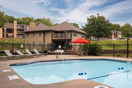 The Tanglewood swimming pool is located in the backyard of the apartment complex, complete with lounge chairs, a red umbrella on a table with chairs, inviting residents to relax and enjoy the summer.