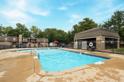 The Tanglewood swimming pool, nestled within the apartment complex, offers a refreshing escape for residents. Enjoy the poolside amenities, including lounge chairs, a table with chairs, and a red umbrella, with the backdrop of the surrounding apartments.