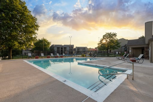 Poolside at The Lakes, showcasing lounge chairs, a table with chairs, and a sparkling pool.