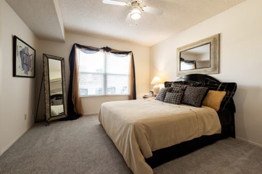Cozy bedroom with a dark wood bed and mirror, beige walls, neutral-colored bedding, a window bringing in natural light, and carpeted floors.