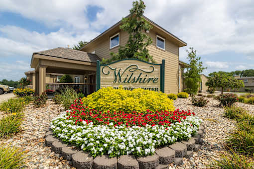Exterior view of the Wilshire clubhouse, featuring a large building with a welcoming entrance, wide windows, and surrounding landscaping,