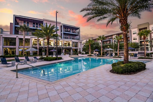 a swimming pool in front of a building with palm trees