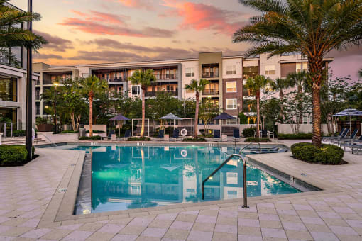 a swimming pool in front of an apartment building at sunset