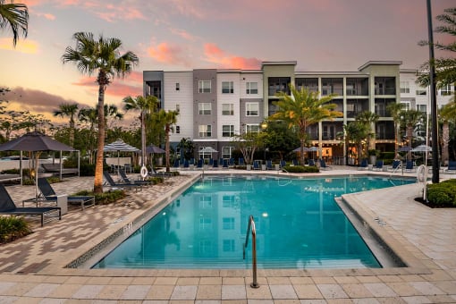 a swimming pool in front of an apartment building at sunset