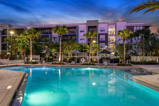 a swimming pool at night with a hotel in the background