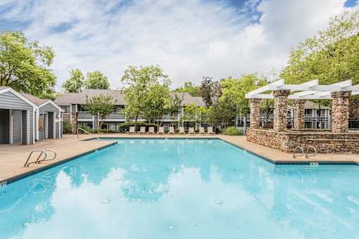 A large swimming pool surrounded by trees and a stone building.