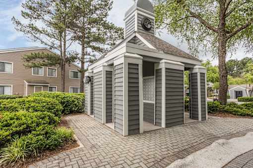 A small grey building with a clock tower sits in the middle of a brick walkway.
