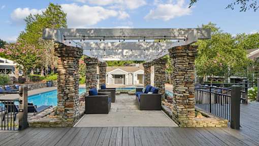 A wooden deck with a stone archway leading to a patio area with a pool.
