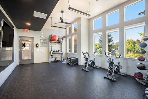 A gym with a black floor and white walls has exercise equipment and windows.