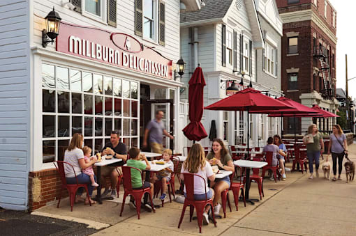 A family is sitting at a table outside of a restaurant called Millburna Delicatessen.