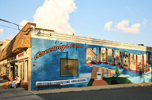 A mural on a building wall with the text "Greetings from Milburn" and "Rest Small Town Around Milburn".