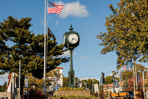 A large clock tower stands in front of a building with a flag flying in the background at The Reserve at Pearl River Apartments, Pearl River, NY