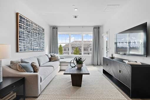 A modern living room with a large window overlooking a house at The Reserve at Pearl River Apartments, Pearl River, New York