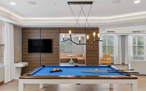 A pool table with a blue cloth and a television mounted on the wall.