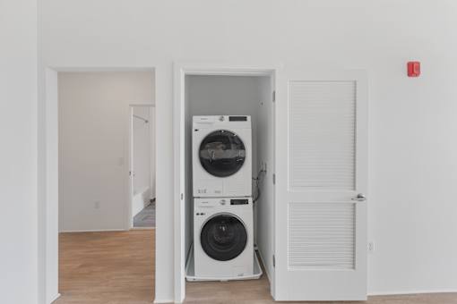 A white door is open to reveal a stacked washer and dryer.