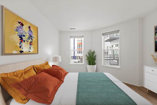 A bedroom with a bed, a painting, a window, and a potted plant.