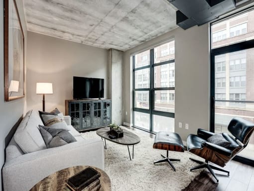 A living room with a grey couch, a wooden coffee table, and a black leather chair at Coda on H Apartments, District of Columbia