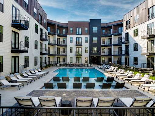 A swimming pool surrounded by lounge chairs in front of apartment buildings.
