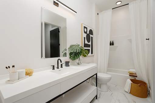 A white bathroom with a sink, mirror, toilet, and a plant at Vintage Edge Nashville Apartments, Nashville, TN