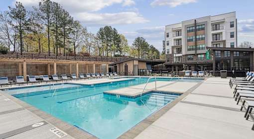 A large outdoor swimming pool with lounge chairs and a building in the background at Vintage Raleigh West Apartments, Raleigh, North Carolina