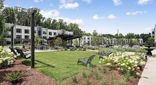 A park with benches and flowers in front of apartment buildings at Vintage Raleigh West Apartments, North Carolina, 27607