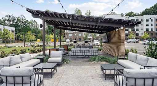 A patio with grey couches and a wooden pergola at Vintage Raleigh West Apartments, Raleigh, NC