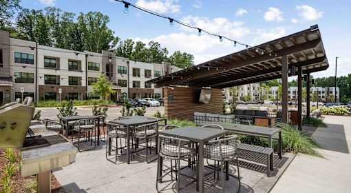 A sunny day at a modern outdoor seating area with tables and chairs at Vintage Raleigh West Apartments, Raleigh, NC