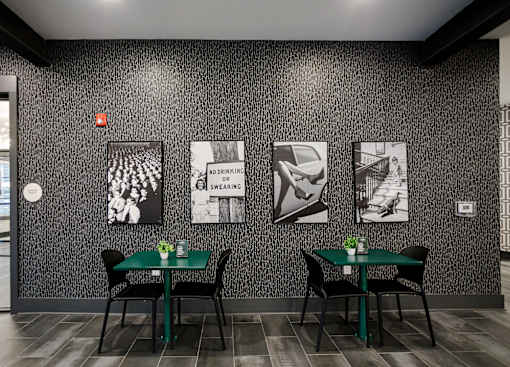 A black and white photo is on the wall above a table with a green tablecloth and two chairs.