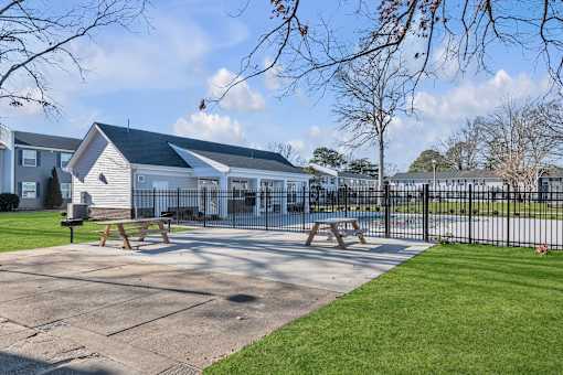 A playground area with a picnic table and a fence in front of a building.