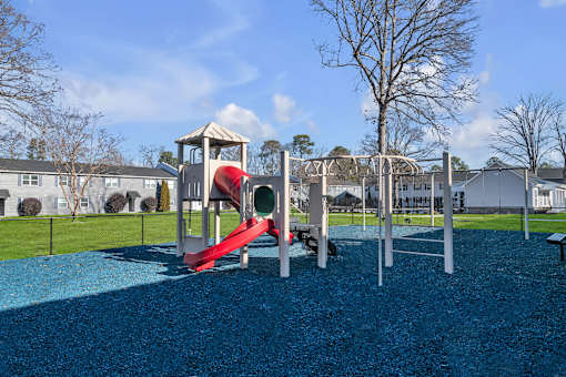 A playground with a red slide and a blue rubberized surface.