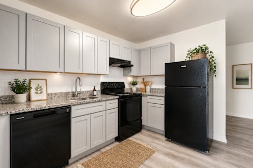 A black refrigerator stands in a kitchen with white cabinets and a black dishwasher.