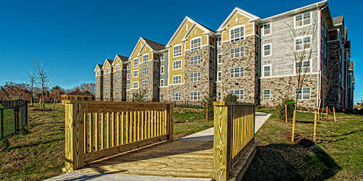 A wooden gate leads to a grassy area in front of a large apartment building at Chapel Springs Apartments, Perry Hall