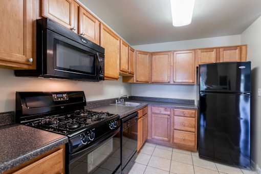A kitchen with black appliances and wooden cabinets at Charlestowne North Apartments, Greenbelt