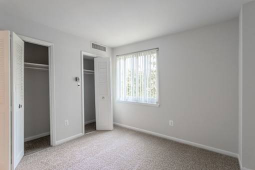 A white bedroom with a window and a carpeted floor at Charlestowne North Apartments, Greenbelt