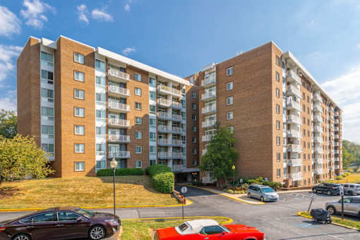 A red car is parked in a parking lot in front of a brick apartment building at Charlestowne North Apartments, Greenbelt, MD