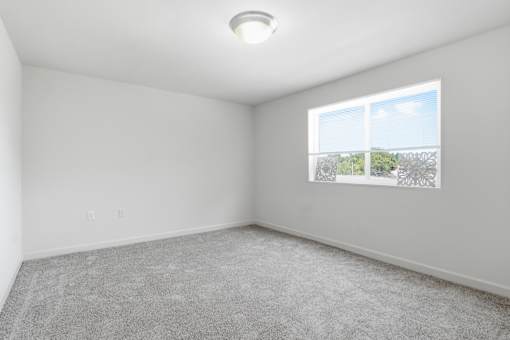A room with a carpeted floor and a window showing a view of trees and a cloudy sky.