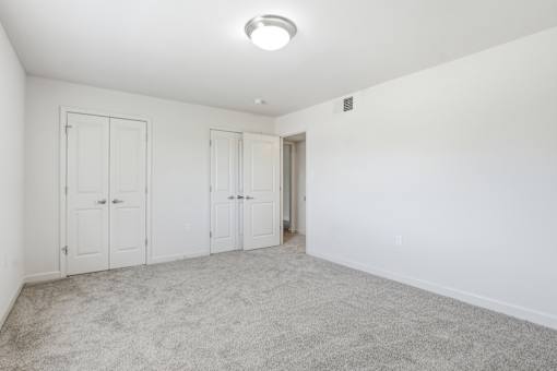 A room with white walls and carpeted floor with four doors.