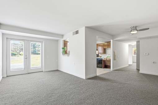 A spacious living room with a grey carpet and white walls.