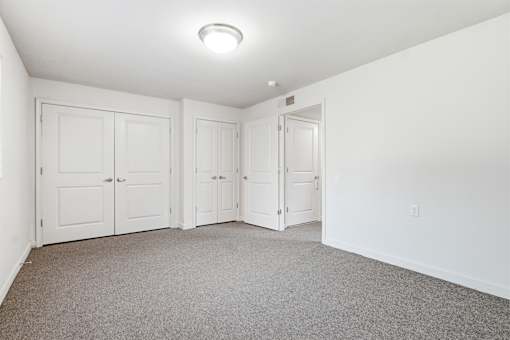 A room with white walls and a carpeted floor with four doors.