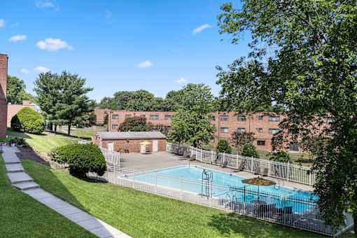 A pool surrounded by a fence and trees in front of a brick building.