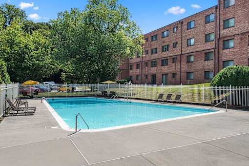 A swimming pool surrounded by a fence and trees in front of a brick building.