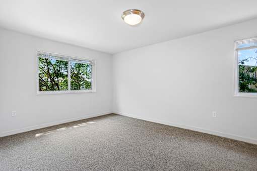 A room with a carpeted floor and two windows.