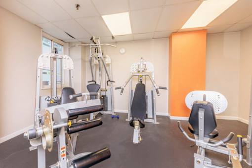 A gym with a variety of equipment including a leg press machine, a chest press machine, a lat pulldown machine, and a leg curl machine at Ashton Heights Apartments, Suitland, MD, 20746