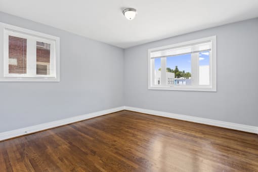 a bedroom with hardwood floors and two windows