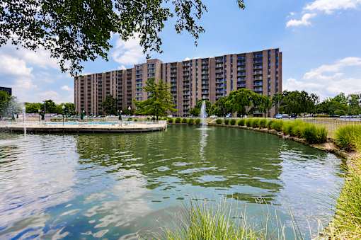 A large building is situated next to a body of water with a fountain in the middle.