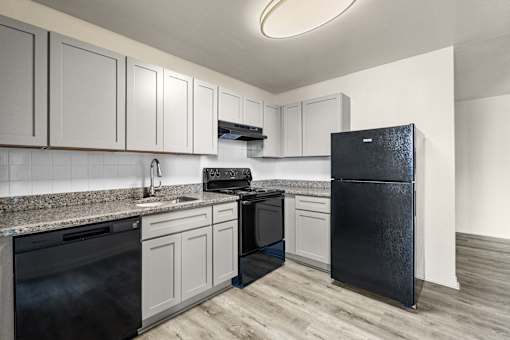 A black refrigerator stands in a kitchen with white cabinets and a black stove.