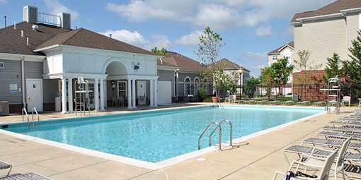 a swimming pool with chairs around it in front of a building at Windsor Crossing, Suitland, MD 