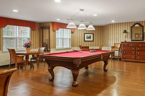 A pool table is in the middle of a room with wood floors and wood paneling on the walls.